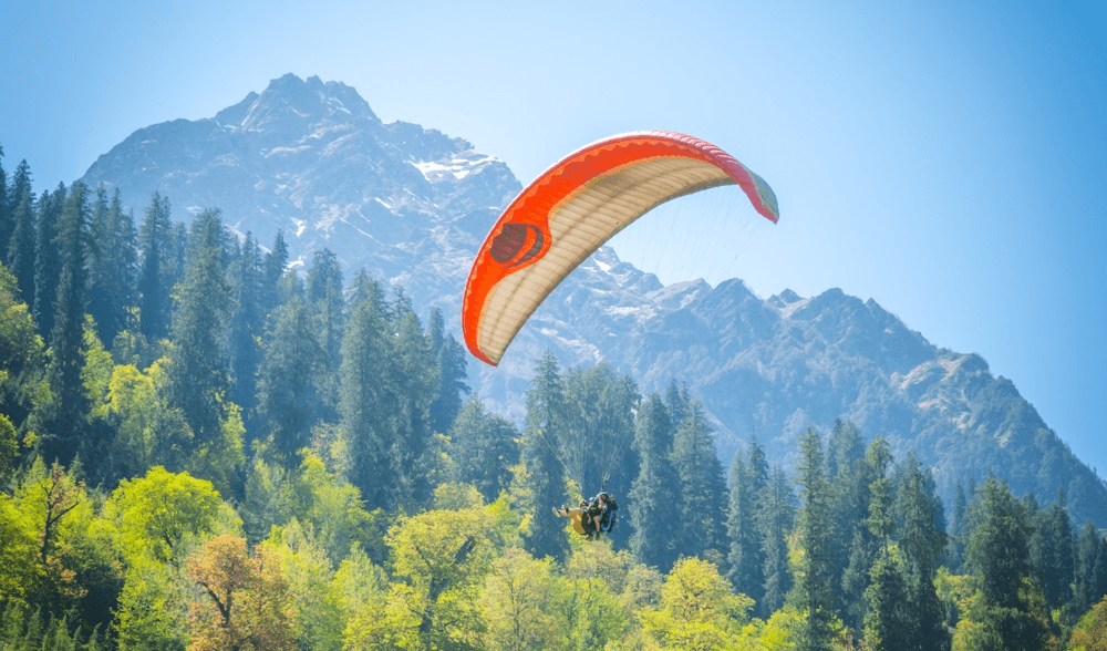 Paraglider flying above a green Himalayan valley